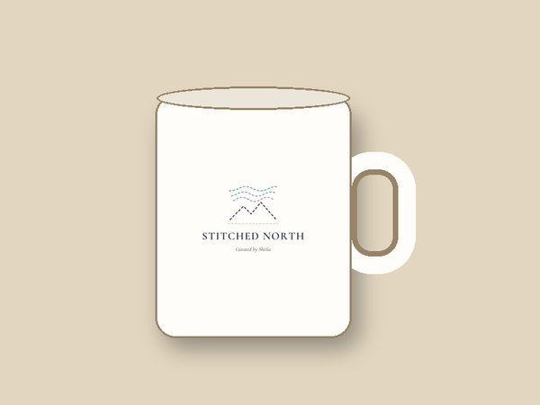 Mockup of a white 11 oz mug on a warm beige background with the Stitched North logo